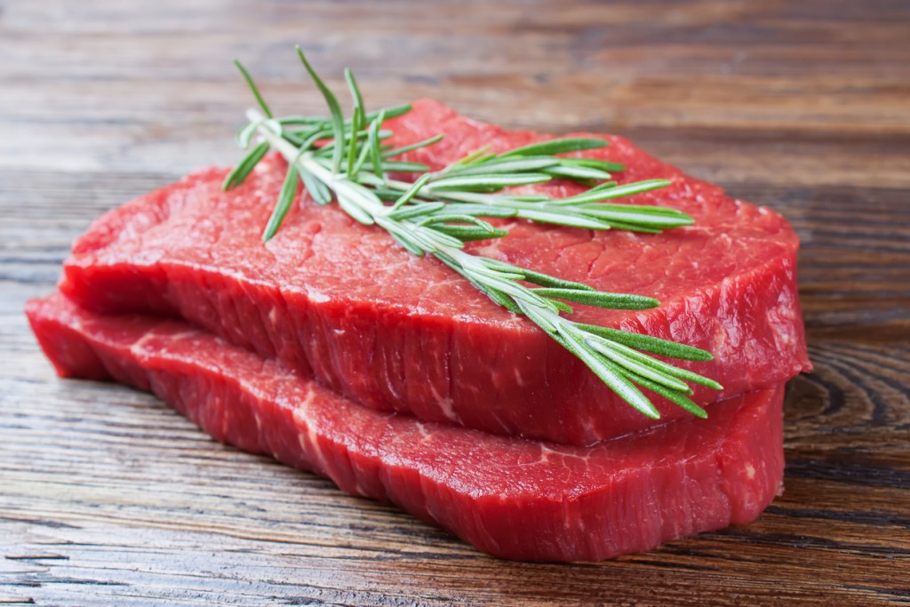 raw beef steak with rosemary on brown wooden background