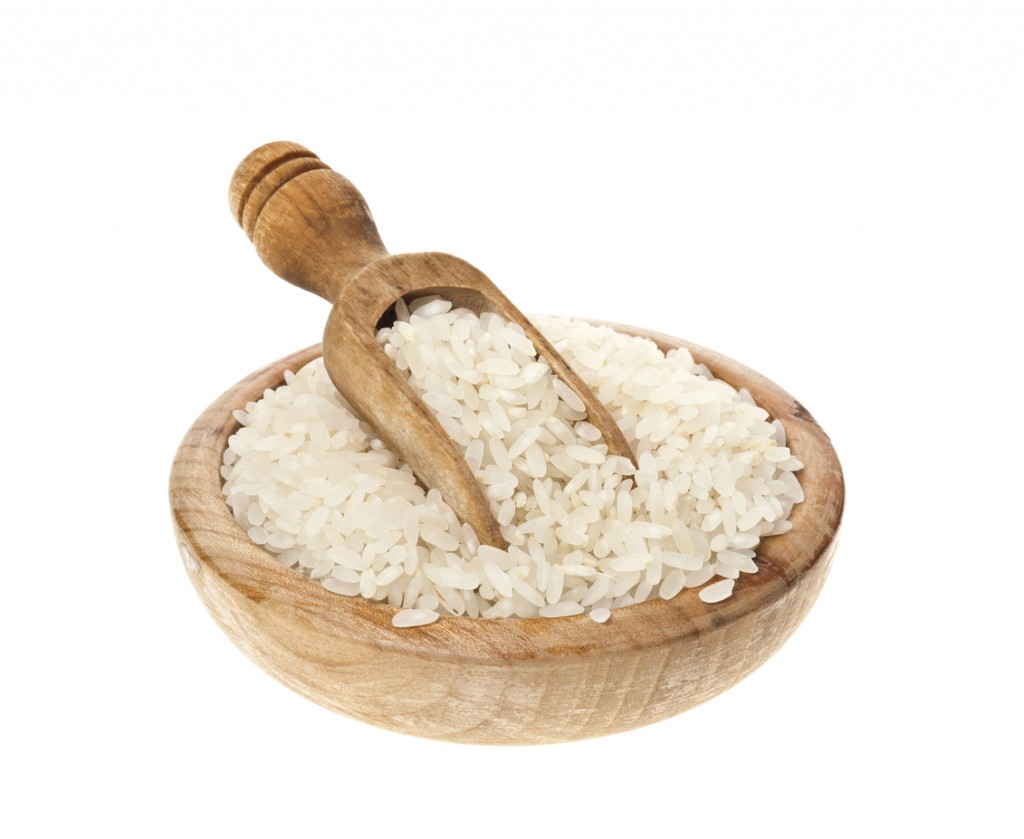 White rice in a wooden bowl and scoop on a white background.