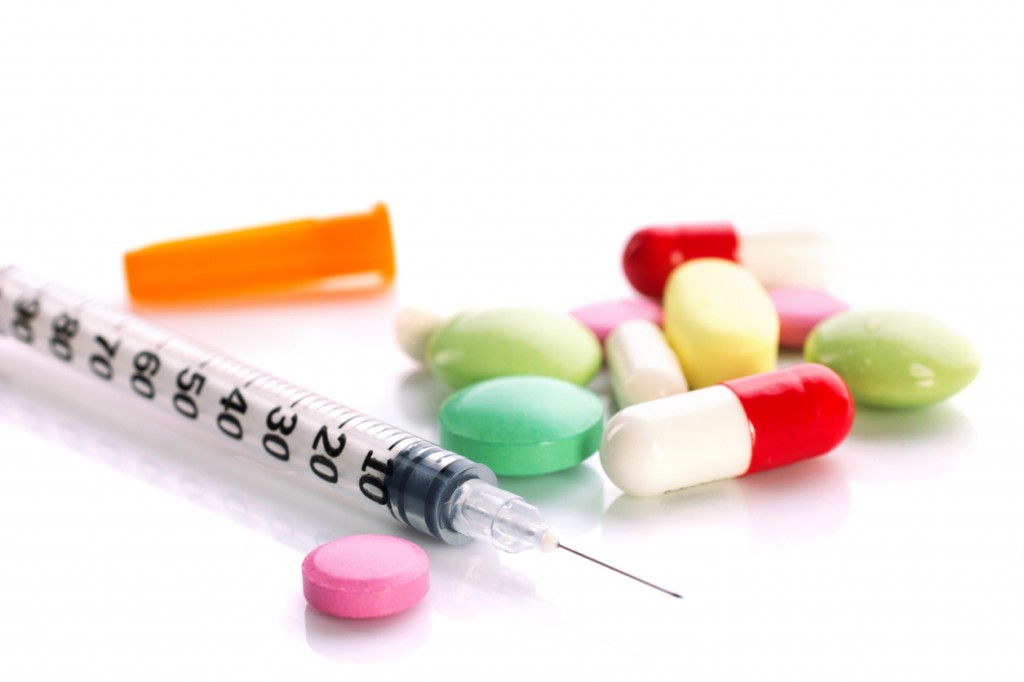 medication in tablets  and capsules and insulin syringe on white and unfocused background