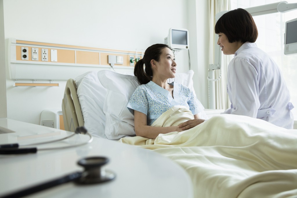 Female doctor sitting on hospital bed and discussing with young female patient