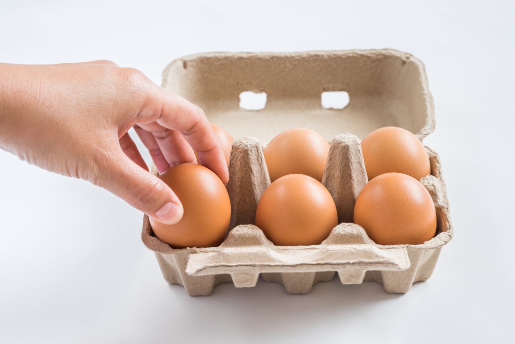 Woman hand selected egg in carton on white background