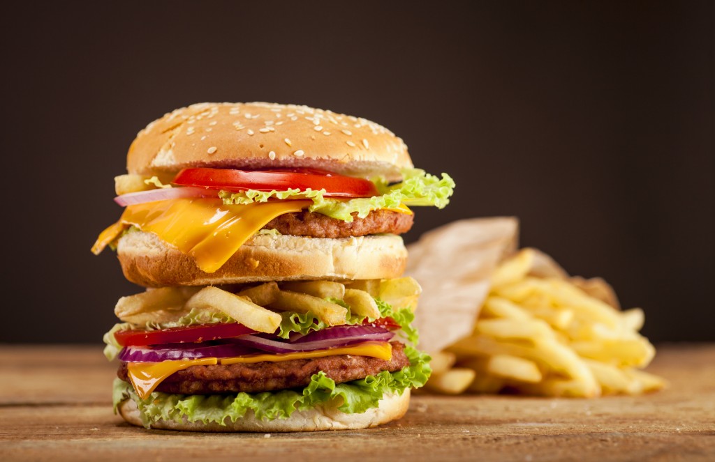 Fresh delicious double burger with cheese, tomato, onion, french fries and lettuce on wooden table and brown background with copy space