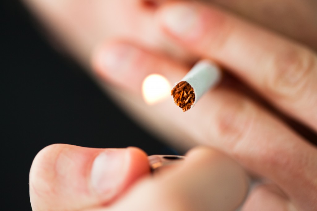 Close up of a man lighting a cigarette against a black background