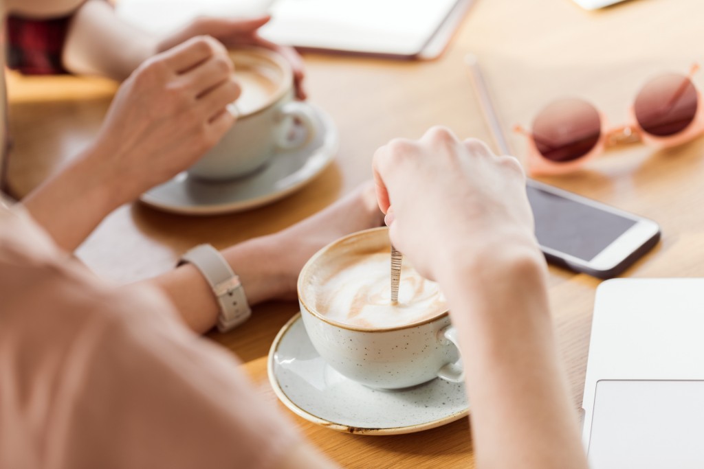 Close-up partial view of young women sitting at table and drinking coffee, coffee break concept