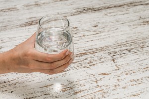 Woman drinking still mineral water from a glass against white wood background. Healthy food, eating, diet, and fitness concept.