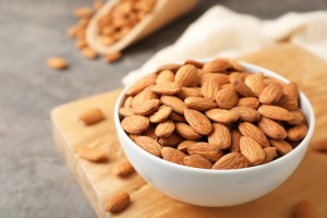 Wooden board with tasty organic almond nuts in bowl on table