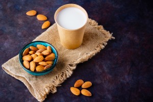 Almond milk with almond on dark background. Homemade organic almond milk in a glass for healthy breakfast. Vegan milk from almonds nuts on a sackcloth. Alternative milk. Top view. Copy space