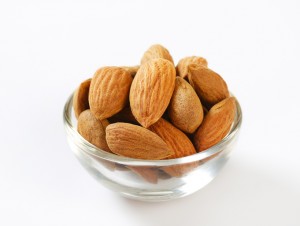 glass bowl of raw almonds on a white background