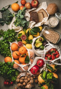 Assortment of vegan, vegetarian, balanced diet foods. Flat-lay of fruit, vegetables, nut, greens and essential rye bread over grey concrete background, top view. Healthy, clean eating