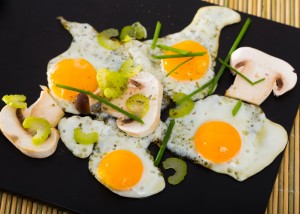 Fried quail eggs with mushrooms, chives and celery on wooden table
