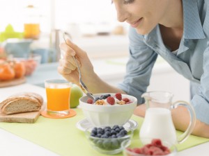 Smiling woman having an healthy delicious breakfast at home, she is eating yogurt with cereals and fresh fruit, healthy lifestyle concept