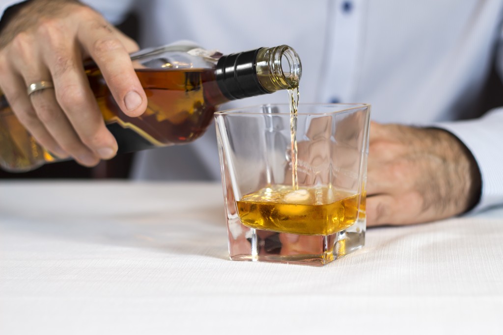 A male hand pours whiskey from a bottle into a glass of ice.