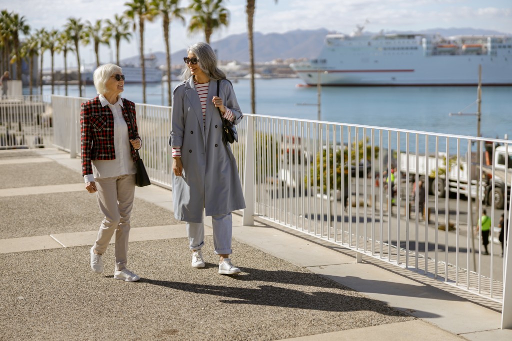 Positive senior women in stylish garments talking while walking along modern city street on autumn day