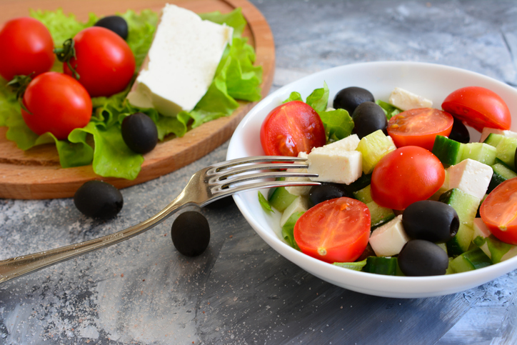 greek salad in bowl with tomatoes, black olives, feta and salad greens and fork, close-up