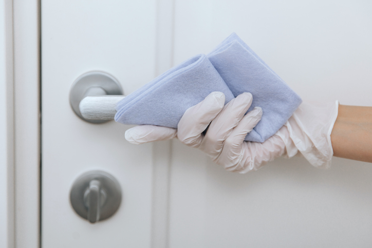 Cleaning door handle with blue wipe in white gloves. Sanitize surfaces prevention in hospital and public spaces against corona virus. Woman hand using towel for cleaning home room door link.