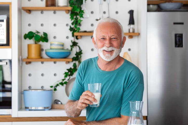 Senior man drinking a glass of milk with a happy face standing and smiling. Handsome senior man drinking a glass of fresh milk in the kitchen