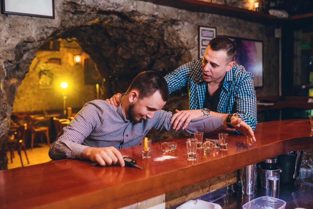 Young man not letting his drunk friend at the bar drive.