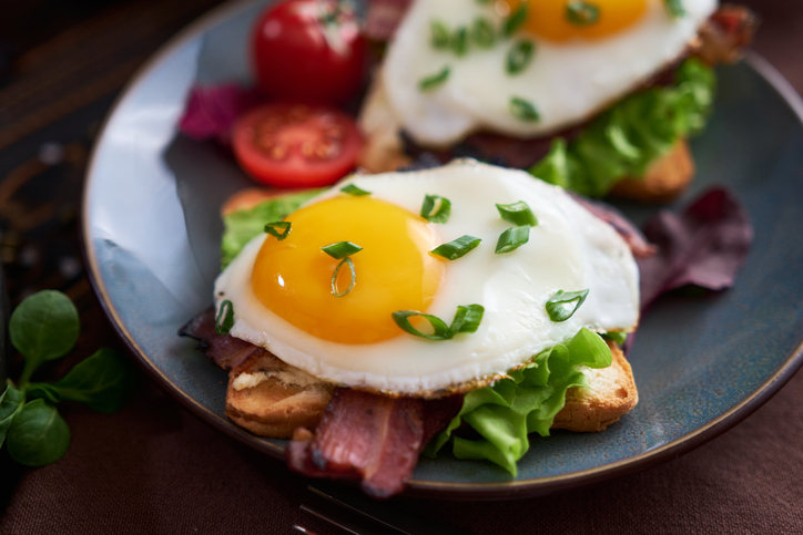 Tasty breakfast - fried egg toasts, bacon, tomatoes on wooden kitchen table.