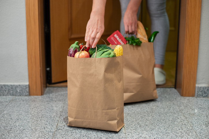 A woman picks up a bag of food at the door of her house. Coronavirus. Quarantine. Stay at home, Online shopping. Vegetables and fruits delivery during quarantine and self-isolation.